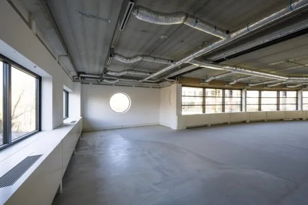 Leeg kantoorpand aan de Wegalaan met betonnen plafond, zichtbare ventilatiebuizen en grote ramen.