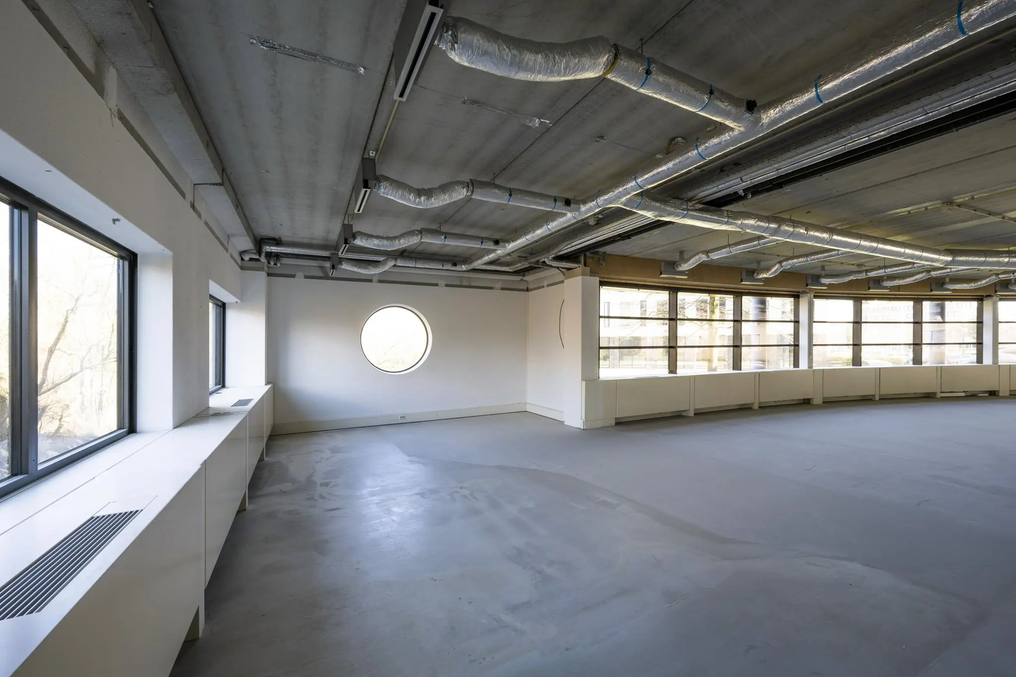Leeg kantoorpand aan de Wegalaan met betonnen plafond, zichtbare ventilatiebuizen en grote ramen.
