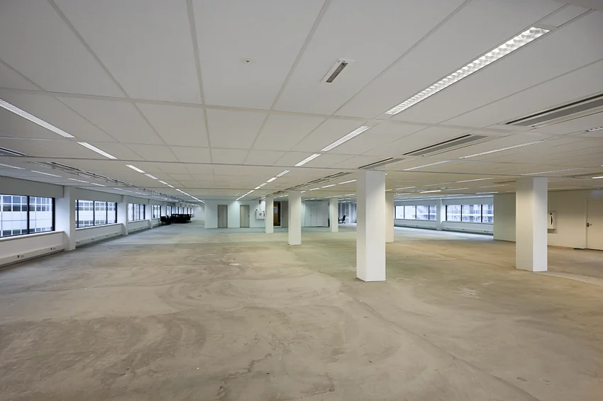Leeg, ruim kantoorpand aan Weena-Zuid met betonnen vloer en systeemplafond.