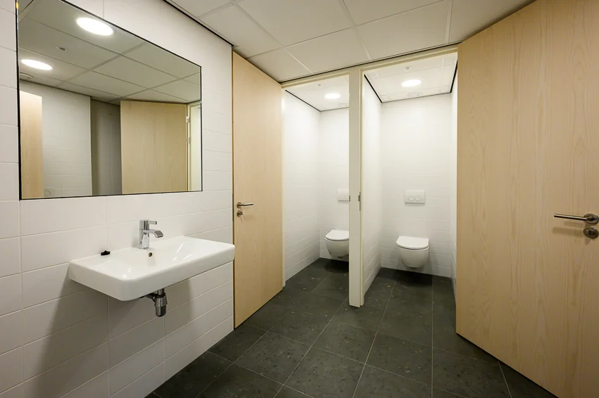 Moderne, strak afgewerkte toiletruimte met twee afgesloten wc-hokjes en een wastafel met spiegel.