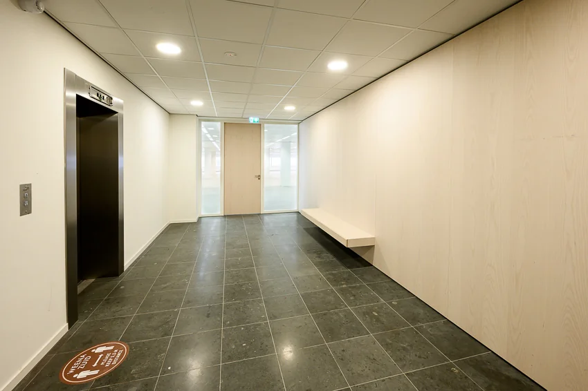 Moderne, lichte kantoorhal in Weena-Zuid met lift, natuurstenen vloer en houten wand met zitbank.