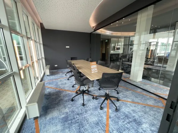 Vergaderruimte in het Rhijnspoorgebouw met glazen wanden, modern meubilair en een blauw tapijt met oranje lijnen.