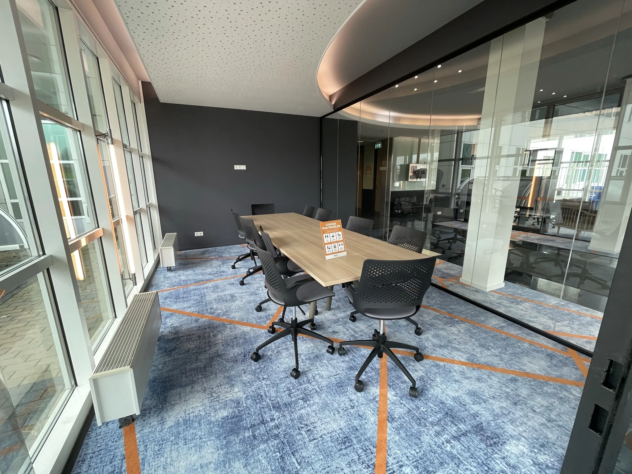 Vergaderruimte in het Rhijnspoorgebouw met glazen wanden, modern meubilair en een blauw tapijt met oranje lijnen.