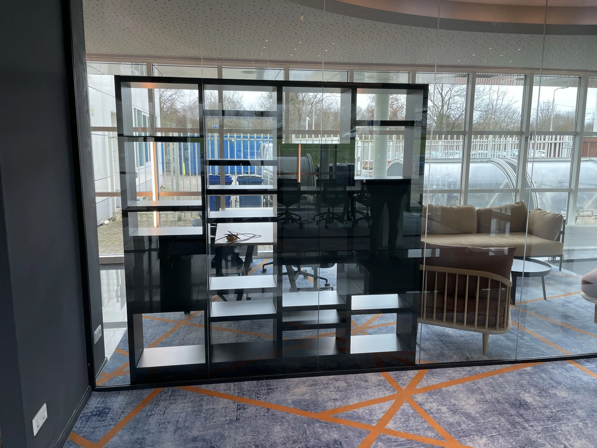 Moderne kantoorruimte met glazen wand, open vakkenkast en zicht op zithoek en buitenomgeving.