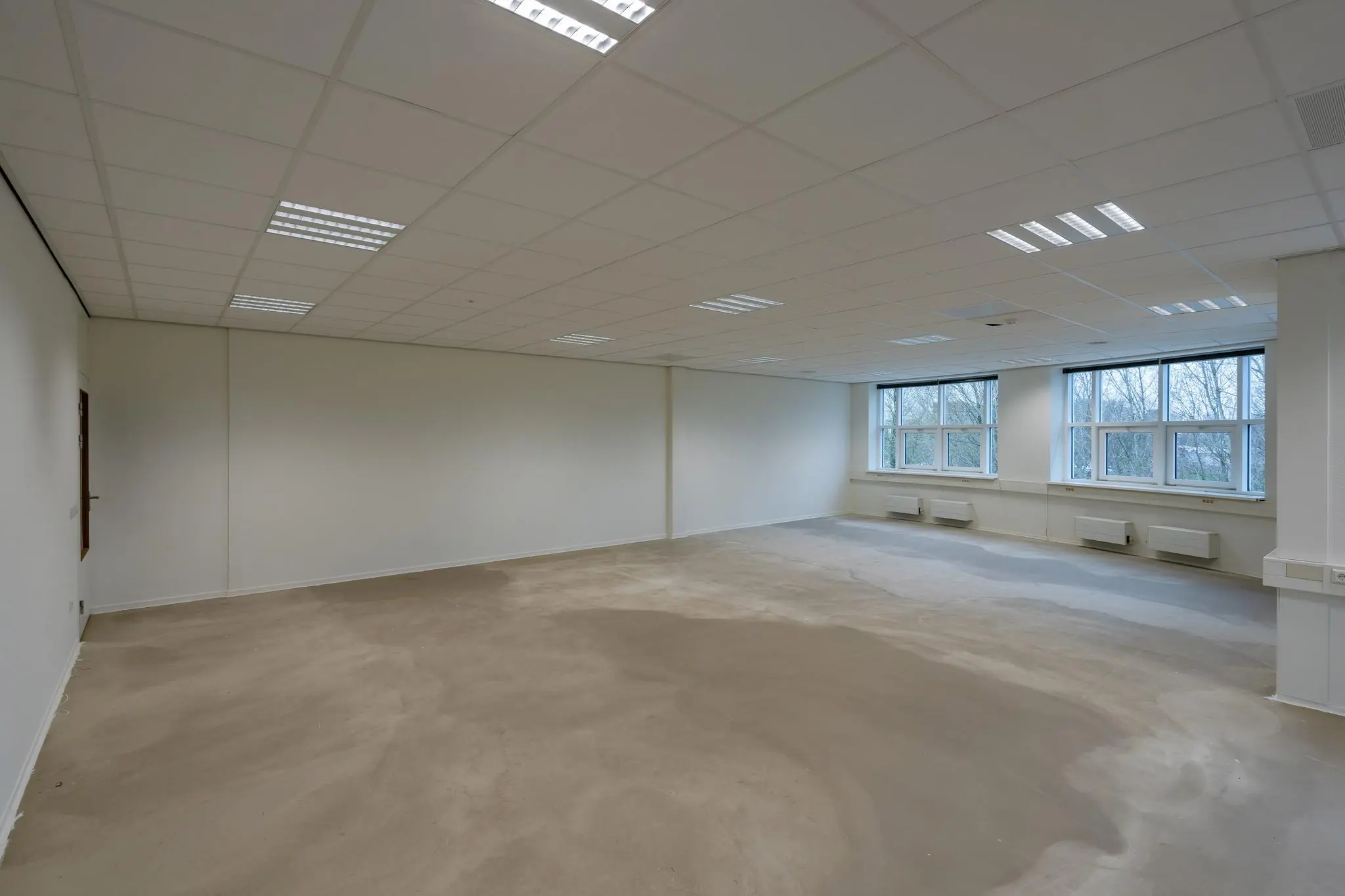 Lege kantoorruimte in het Rhijnspoor-gebouw met systeemplafond, grote ramen en betonnen vloer.
