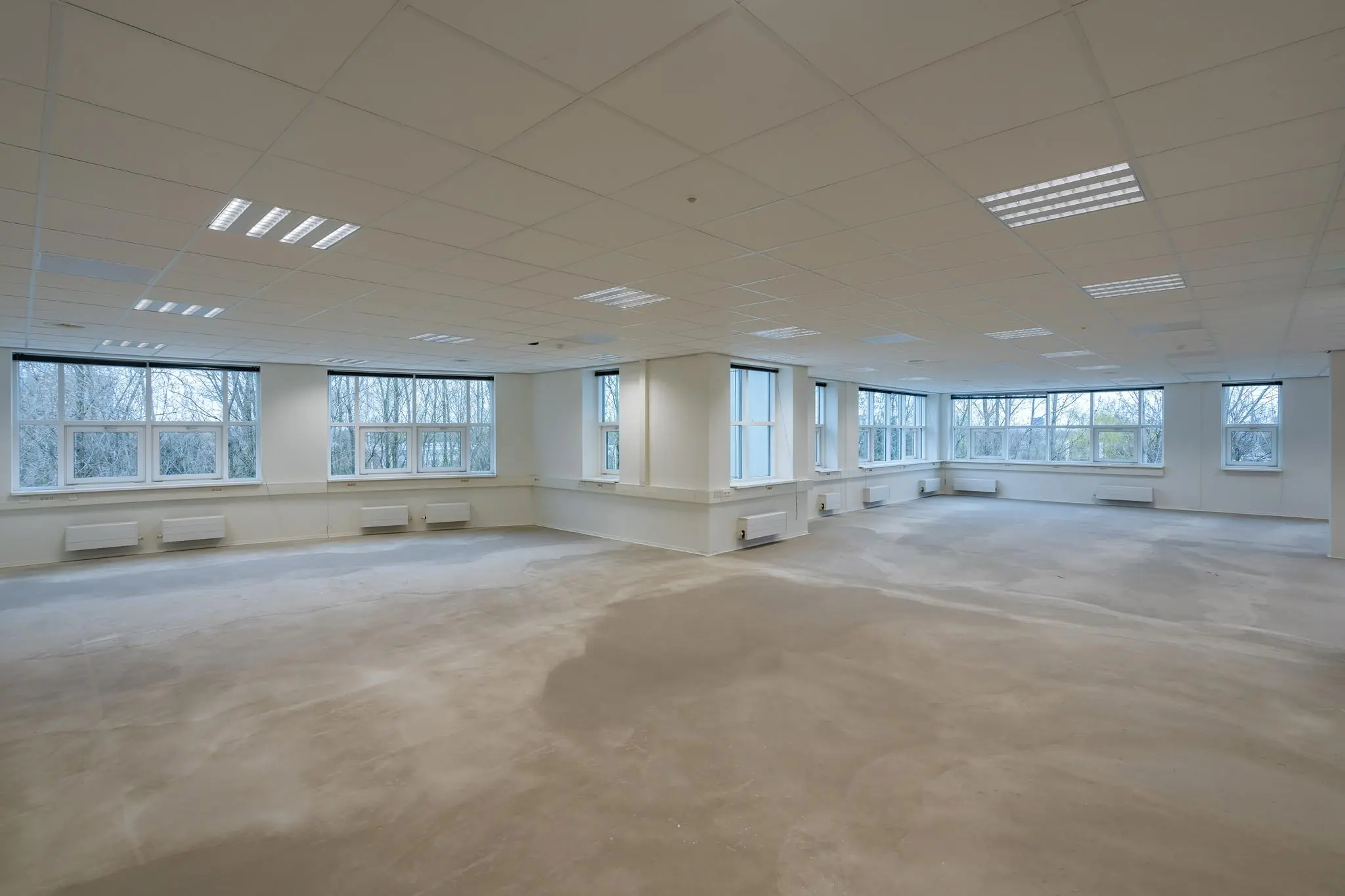 Lege kantoorruimte in het Rhijnspoorgebouw met grote ramen en systeemplafond.