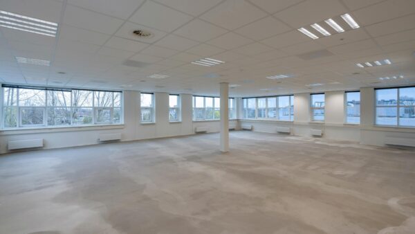 Leegstaande, ruimtelijke kantoorruimte in het Rhijnspoor-gebouw met grote ramen en systeemplafond.