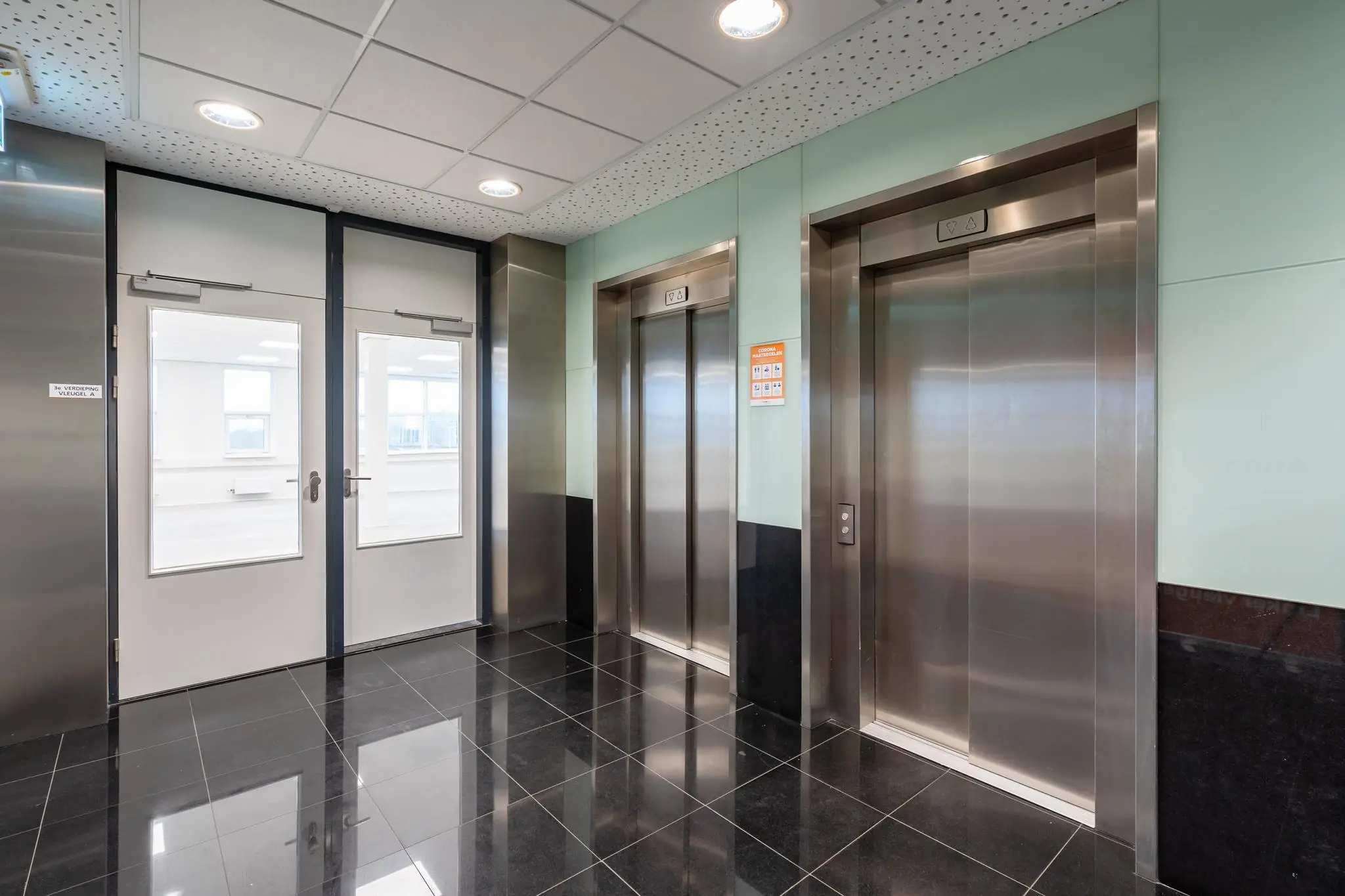 Moderne liftlobby met twee rvs-liften en glazen deuren in kantoorgebouw Rhijnspoor.