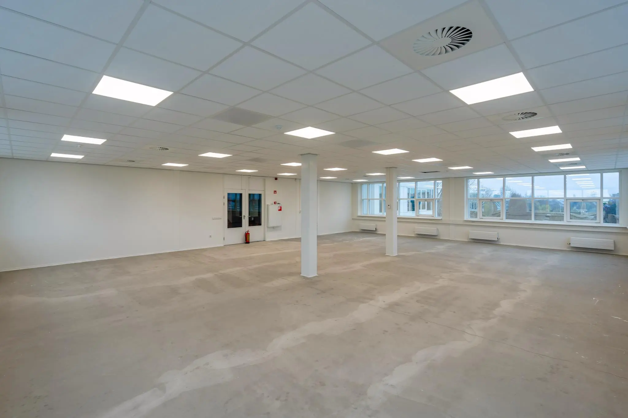 Leeg en licht kantoorpand aan het Rhijnspoor met systeemplafond en grote raampartijen.