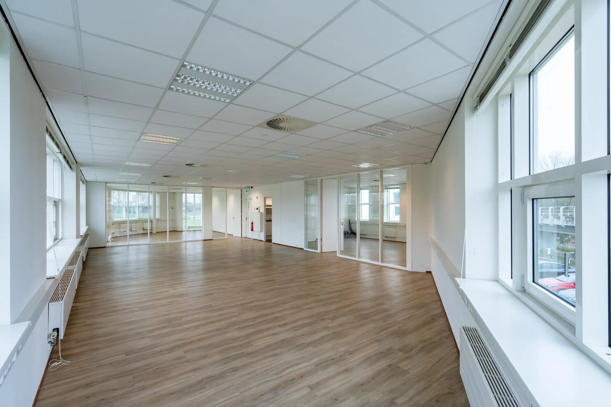 Ruime, lichte kantoorruimte aan het Rhijnspoor met houten vloer, systeemplafond en glazen tussenwanden.