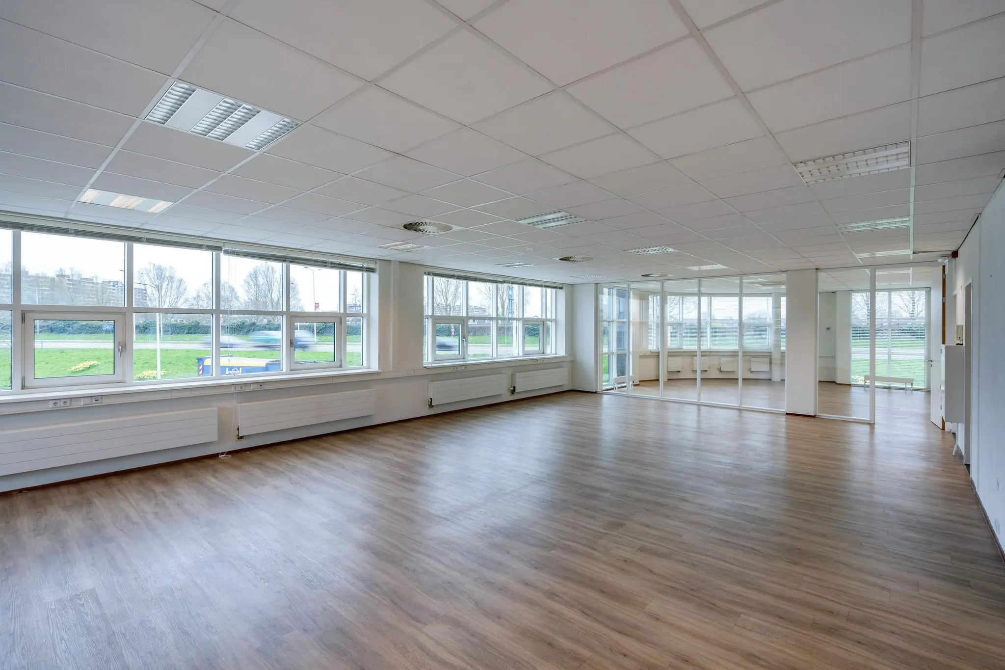 Lichte, lege kantoorruimte met houten vloer en grote ramen aan het Rhijnspoor.