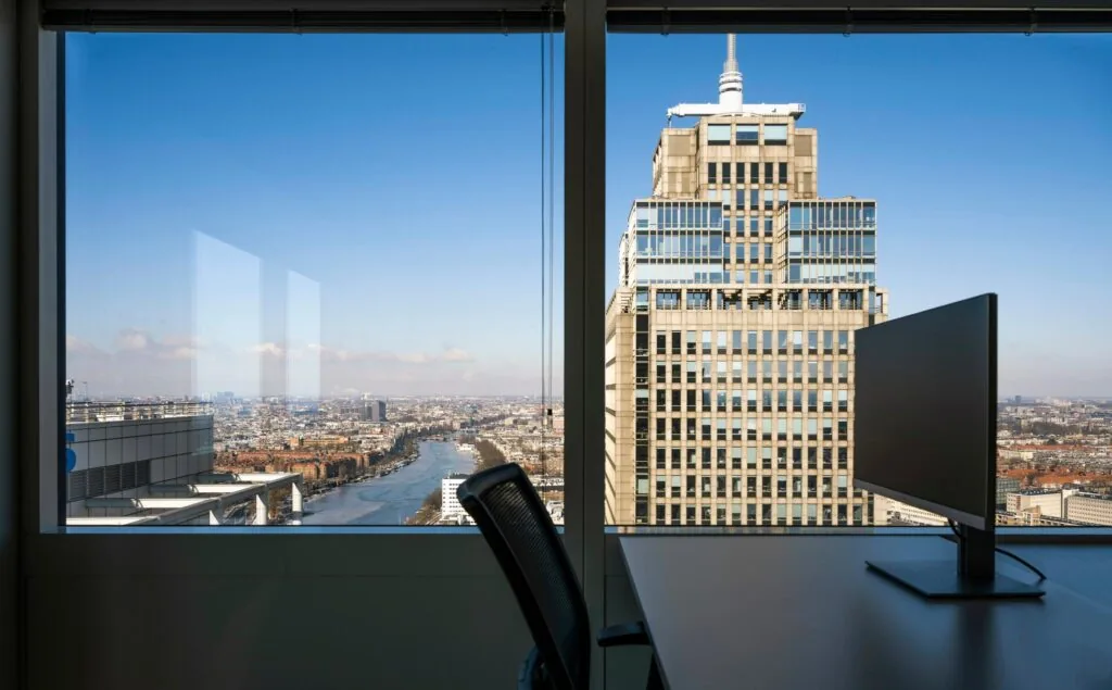 Uitzicht vanuit een kantoor op het Amstelplein in Amsterdam met een groot kantoorgebouw en de Amstel in beeld.