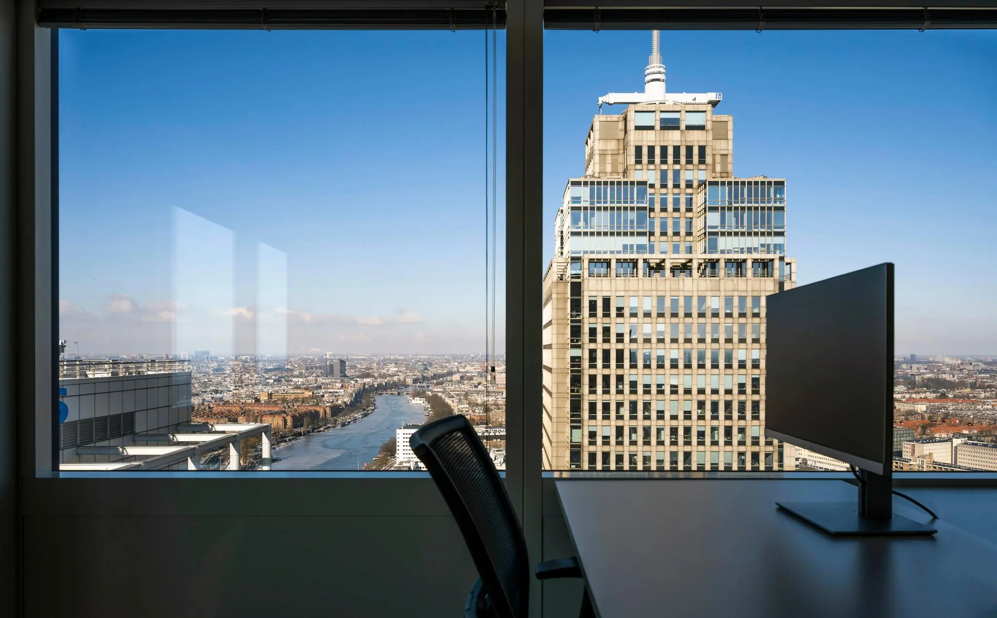 Uitzicht vanuit een kantoor op het Amstelplein in Amsterdam met een groot kantoorgebouw en de Amstel in beeld.