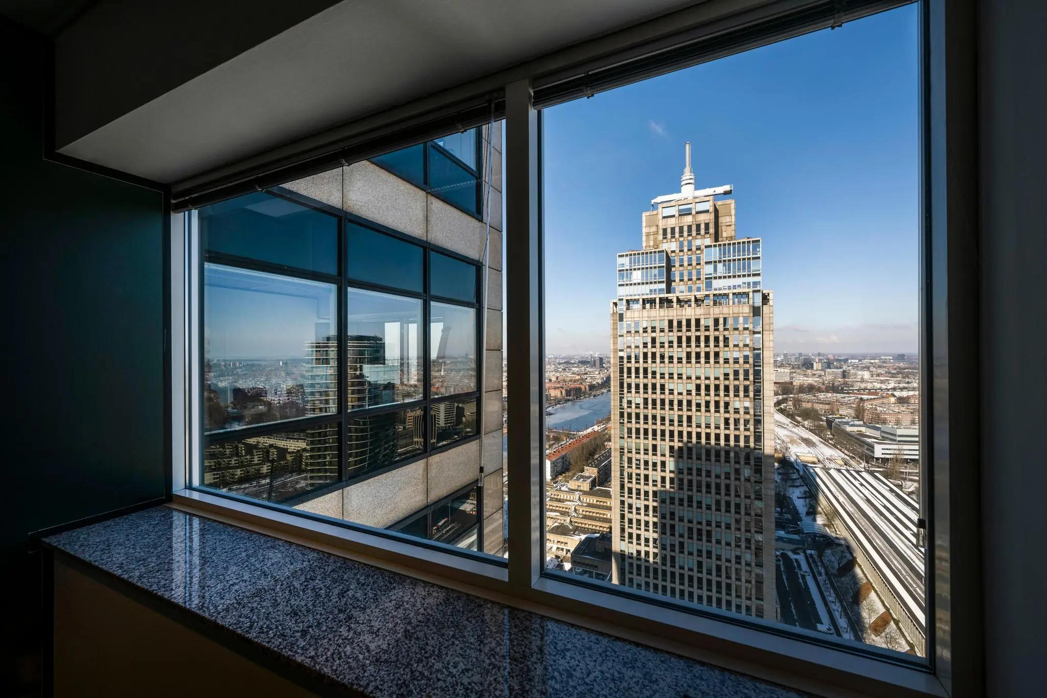 Uitzicht vanuit een raam op het kantoorgebouw aan het Amstelplein in Amsterdam met de Amstelrivier en stad op de achtergrond.