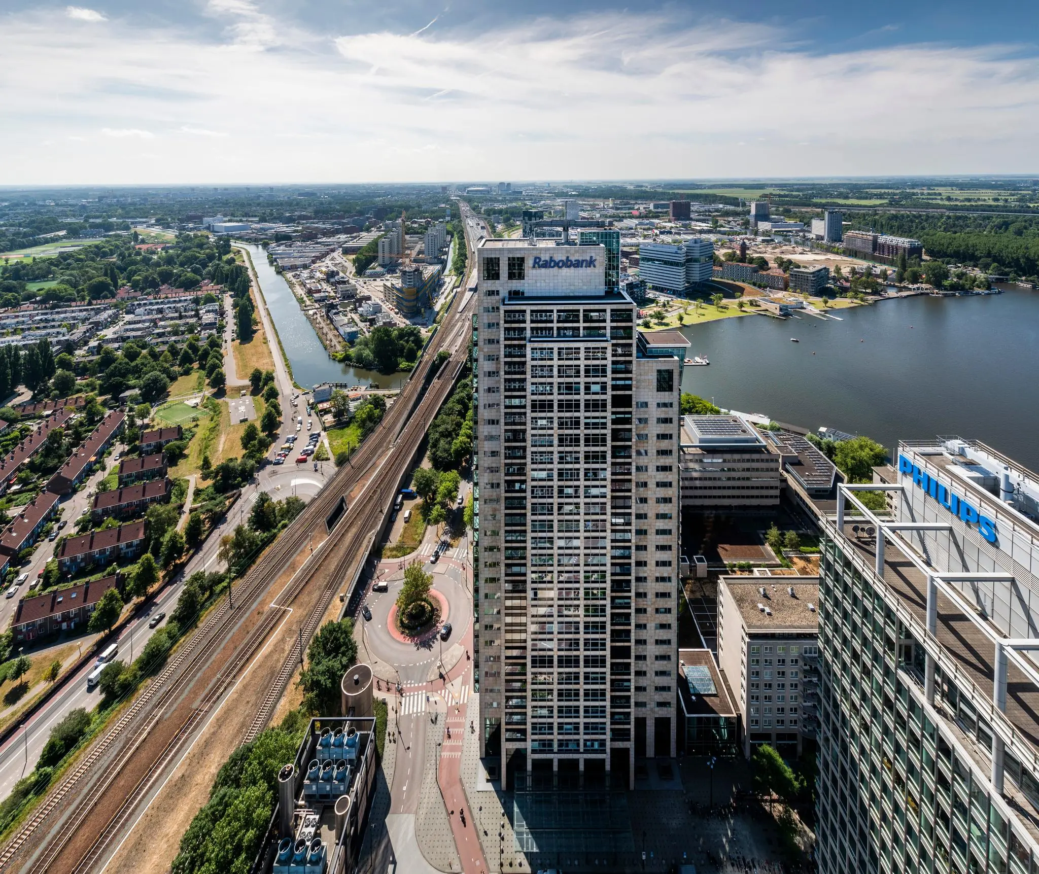 Luchtfoto van het Amstelplein in Amsterdam met de hoge Rabobank- en Philips-gebouwen naast het spoor en de Amstel.