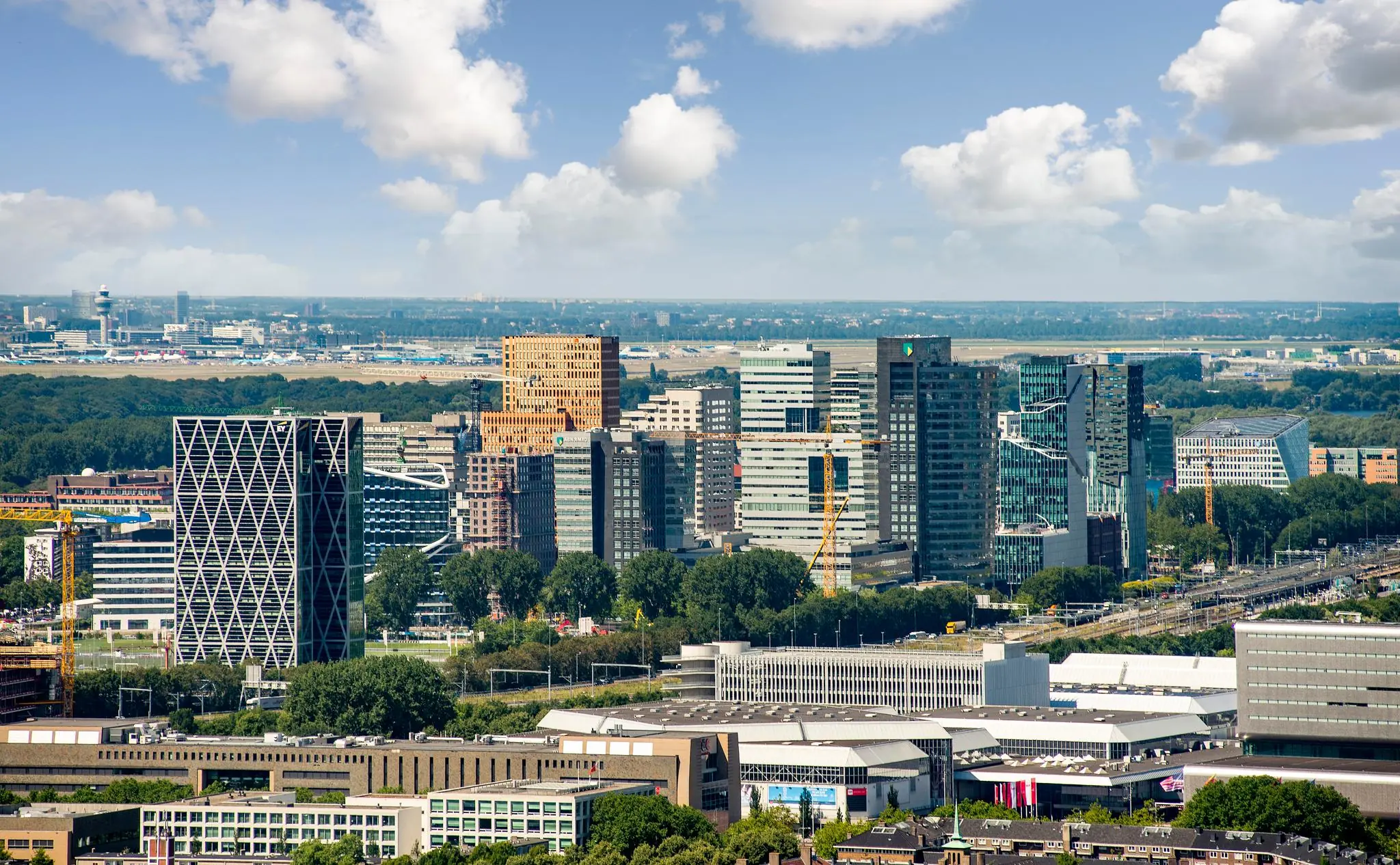 Luchtfoto van de hoogbouw op het Amstelplein in de Zuidas van Amsterdam met moderne kantoorpanden en een helderblauwe lucht.