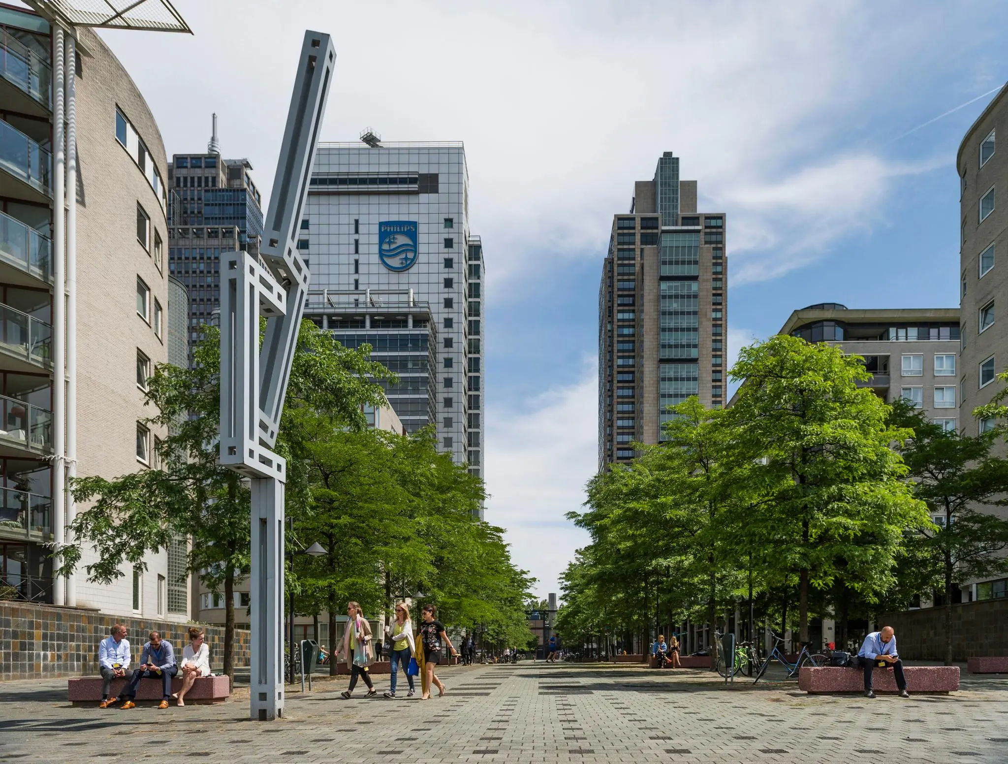 Modern stadsplein Amstelplein in Amsterdam met hoge kantoorgebouwen, waaronder het Philips-gebouw, omringd door bomen en mensen op bankjes.