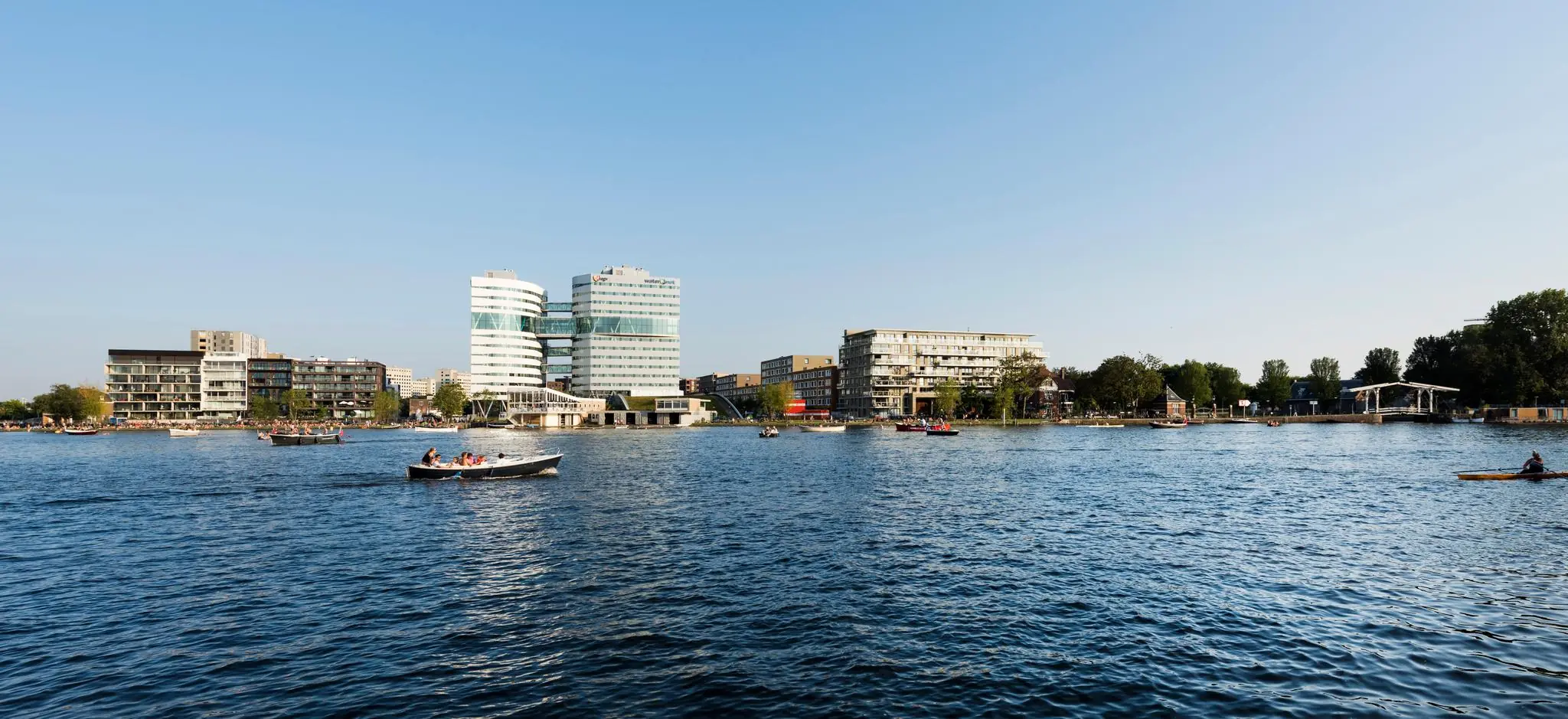 Uitzicht op het Amstelplein in Amsterdam met moderne gebouwen aan het water en bootjes op de rivier.