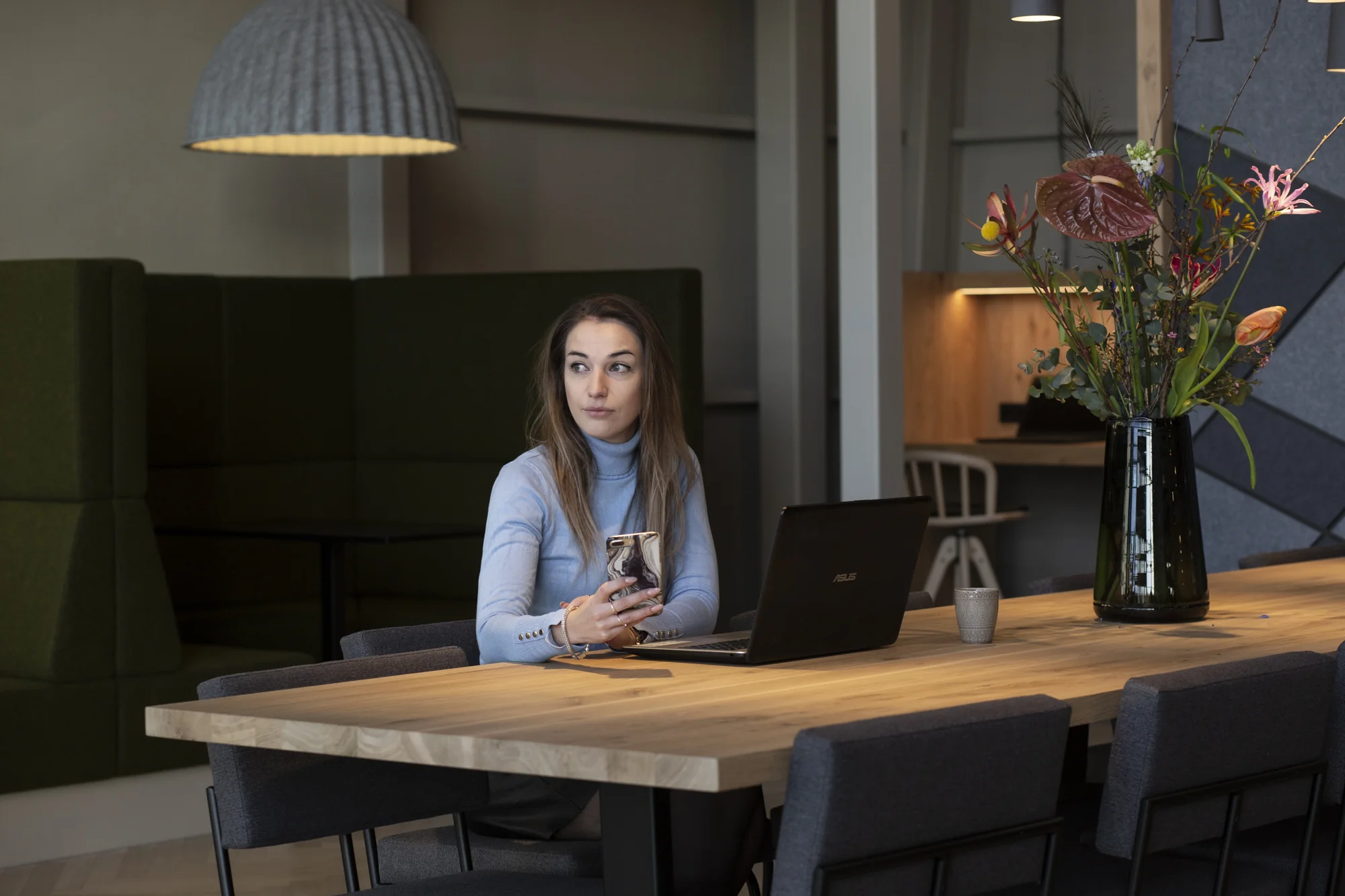 Vrouw met laptop en telefoon zit aan houten vergadertafel in modern kantoor aan de Atoomweg.