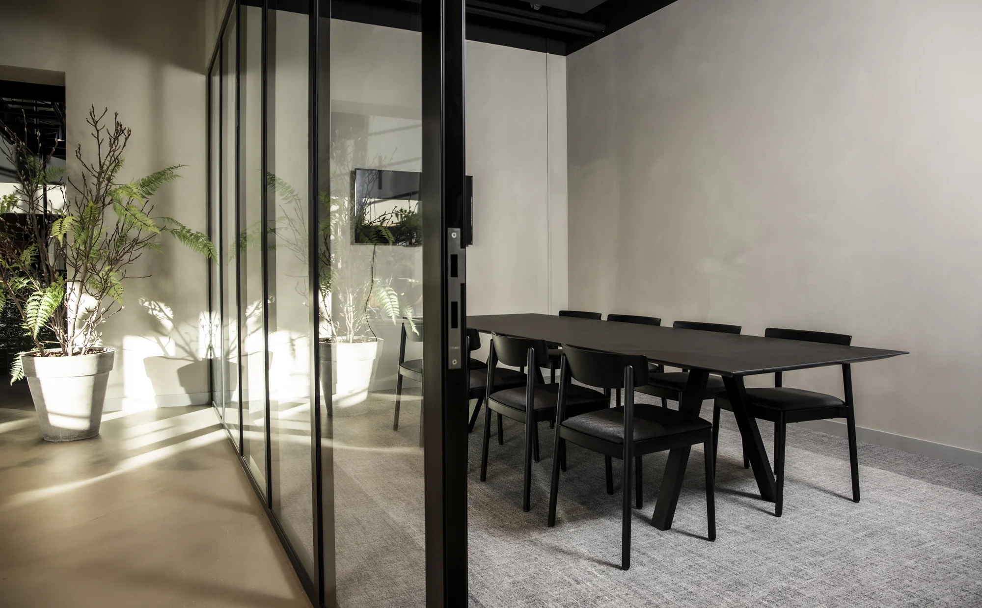 Vergaderruimte aan de Atoomweg met een moderne inrichting, zwarte tafel en stoelen, glazen wand en grote planten.