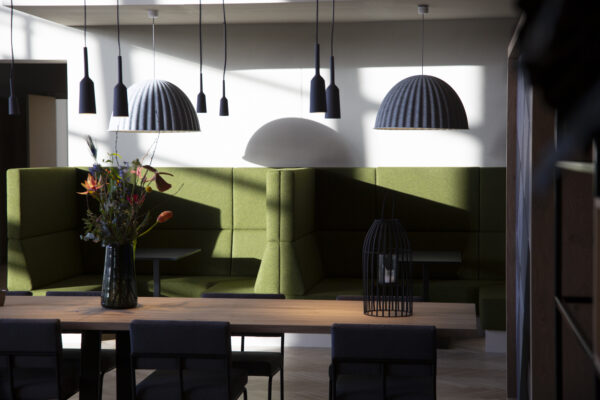 Moderne zithoek met groene banken, houten tafel, hanglampen en een vaas met bloemen in een stijlvol interieur aan de Atoomweg.