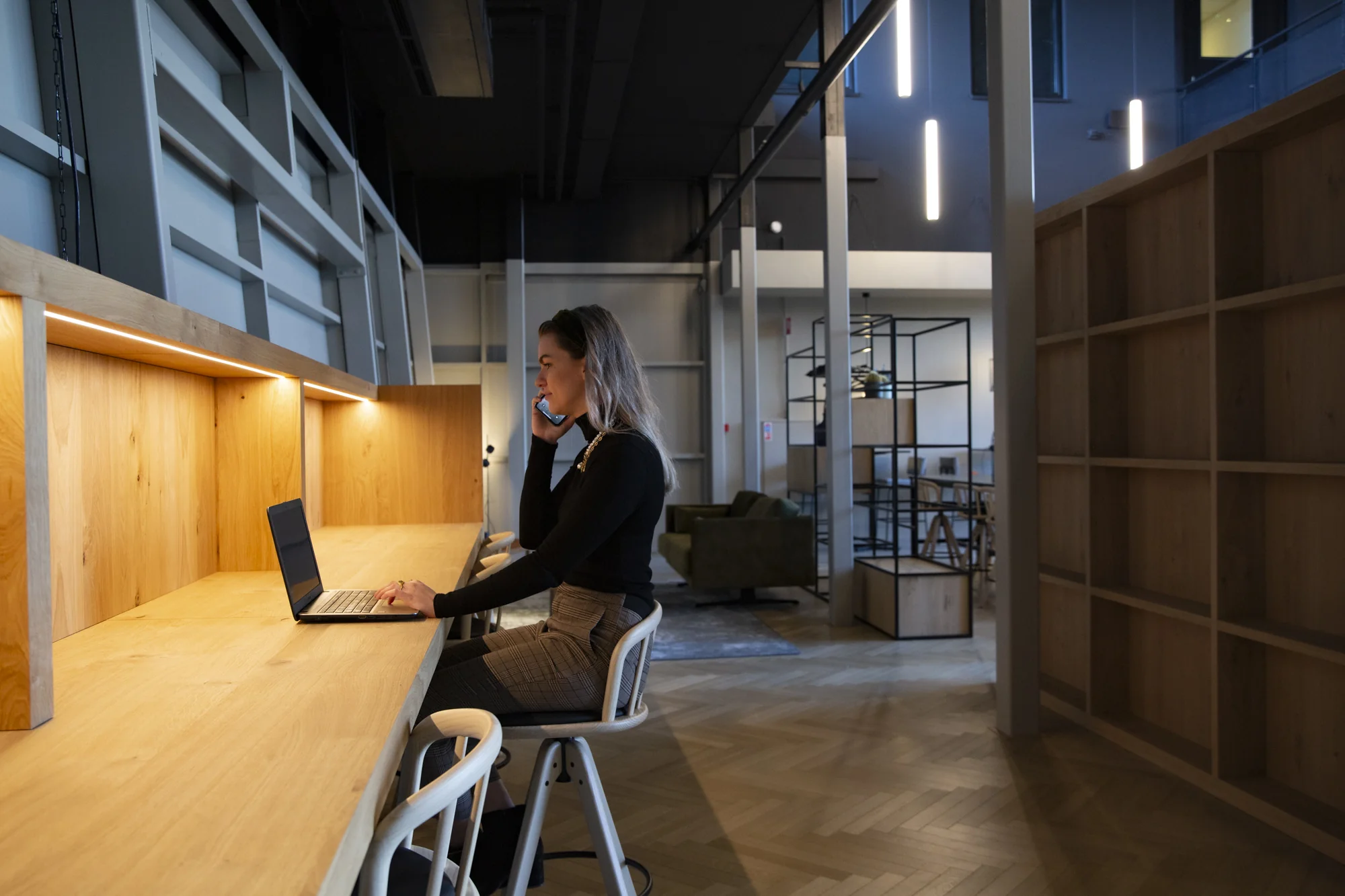 Vrouw werkt met laptop en telefoon aan een houten werkplek in een modern kantoor aan de Atoomweg.