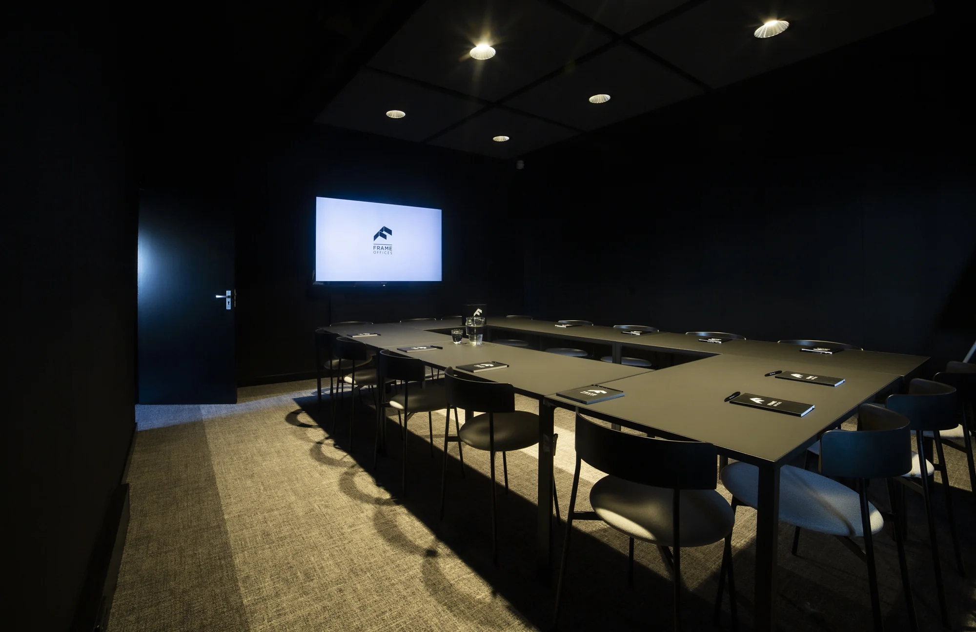 Vergaderruimte bij Frame Offices Atoomweg met donkere inrichting, moderne stoelen en een presentatiescherm.