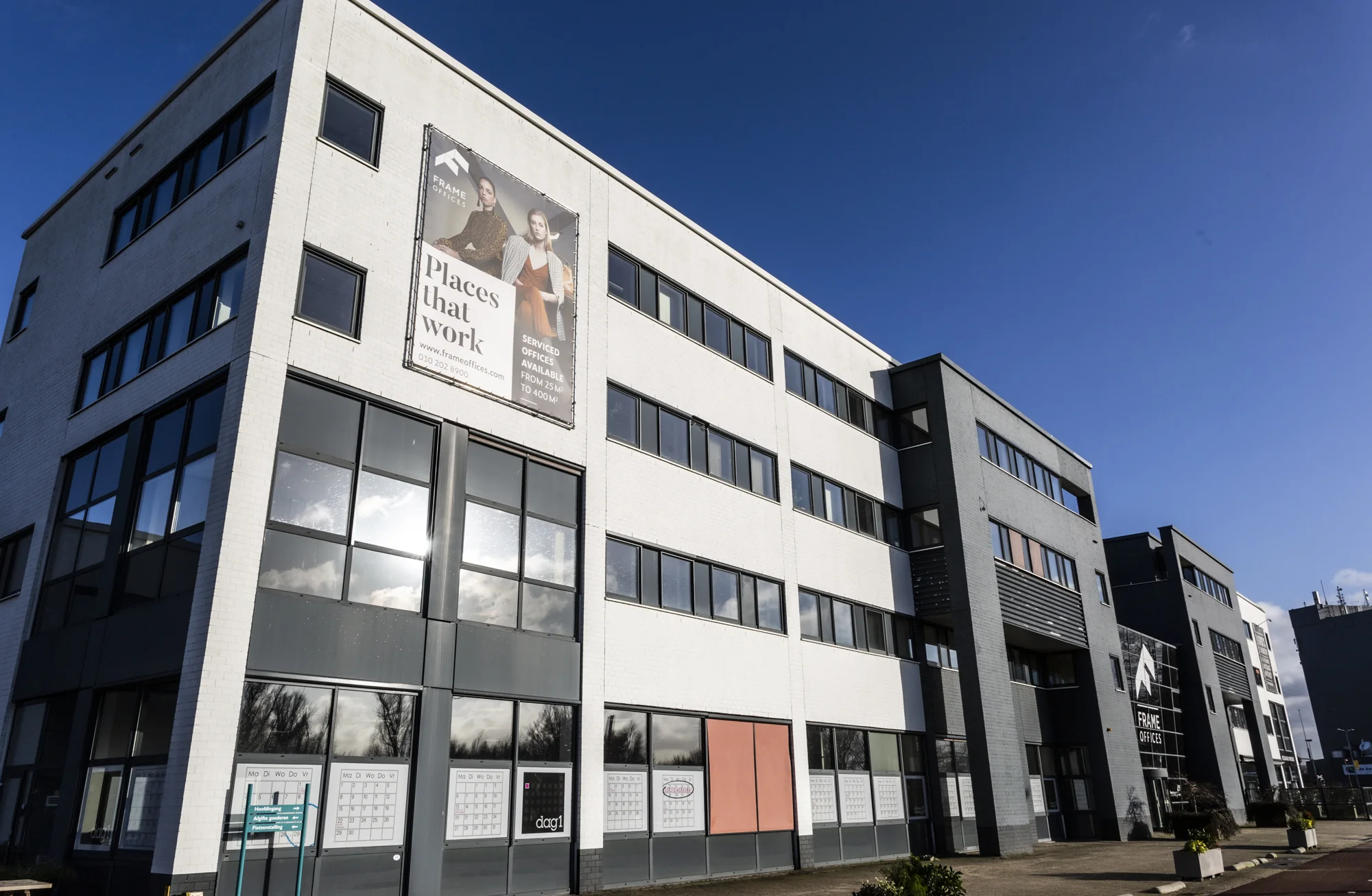 Kantoorgebouw aan de Atoomweg met reclamebanner voor Frame Offices onder een heldere blauwe lucht.