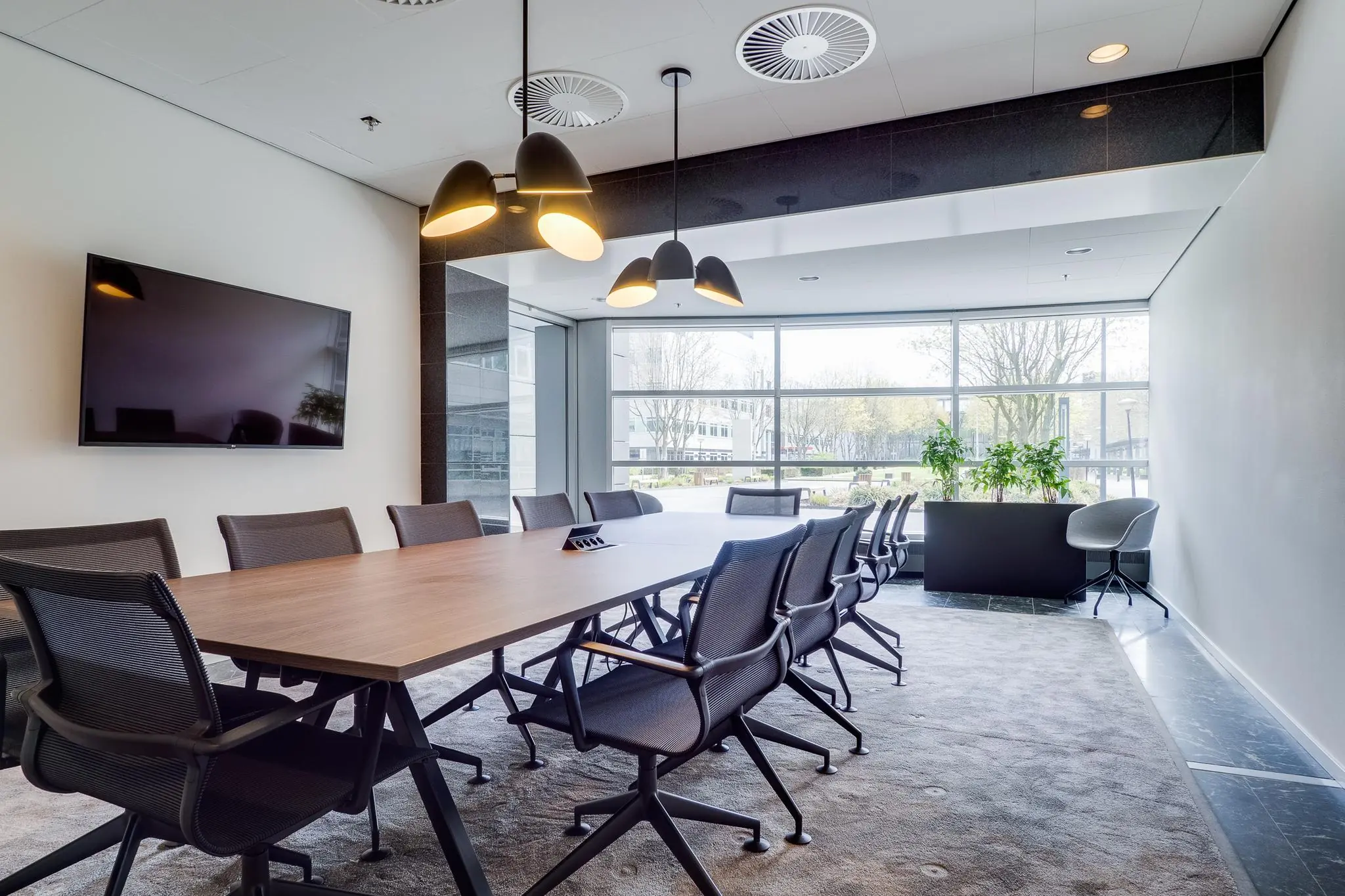 Moderne vergaderruimte aan de Winthontlaan met lange tafel, bureaustoelen, flatscreen en grote raampartij met uitzicht op buiten.