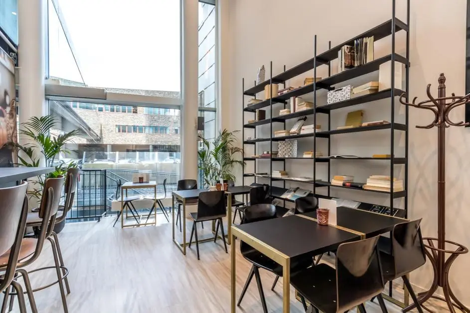 Modern ingerichte lees- en werkruimte met hoge ramen, zwarte tafels, een open boekenkast en uitzicht op Herculesplein.