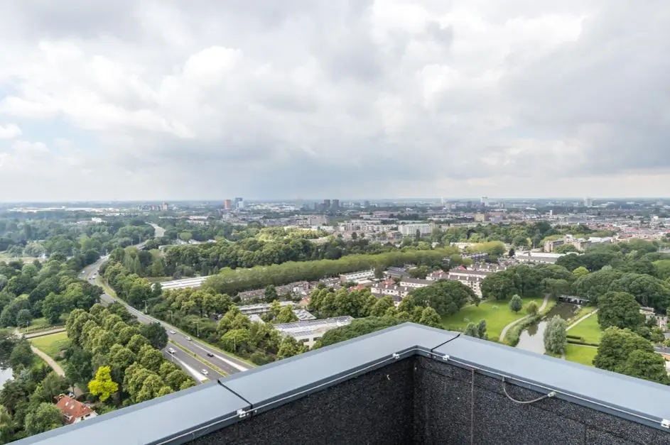 Uitzicht vanaf een hoog gebouw op het Herculesplein in Utrecht met groene parken, wegen en stadsbebouwing onder een deels bewolkte lucht.