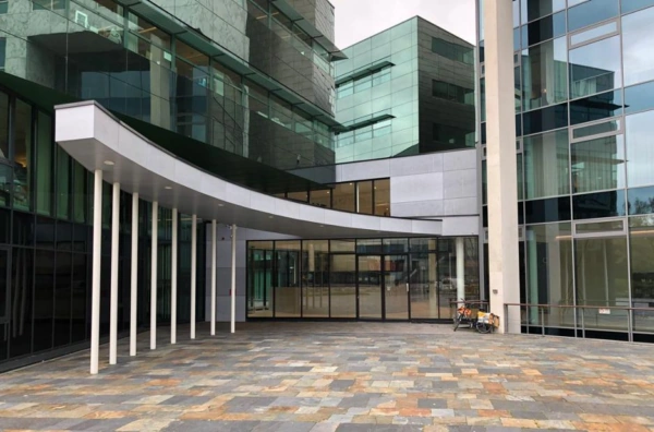 Moderne glazen gevel van een kantoorgebouw aan het Herculesplein met een rond afdak en geparkeerde fiets.