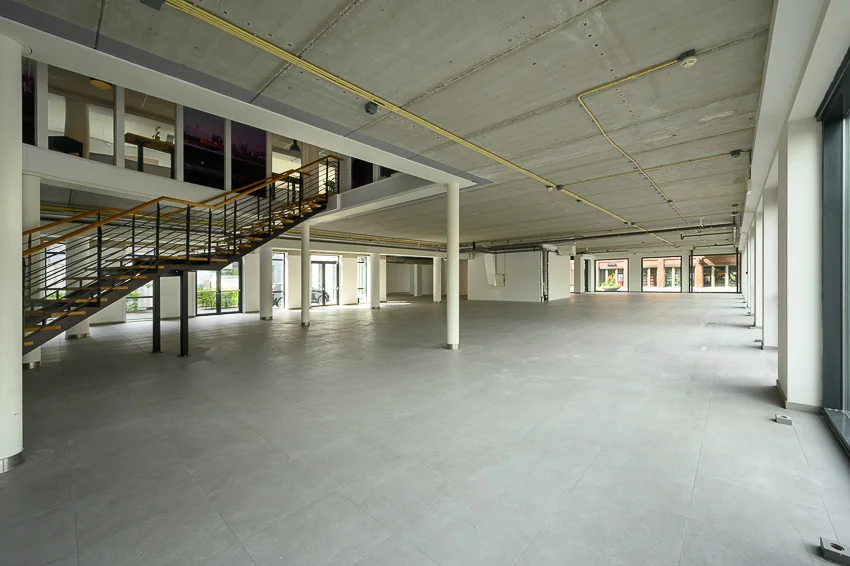 Ruime, lege bedrijfsruimte aan de Haastrechtstraat met betonnen plafond, grijze tegelvloer en een metalen trap naar de bovenverdieping.