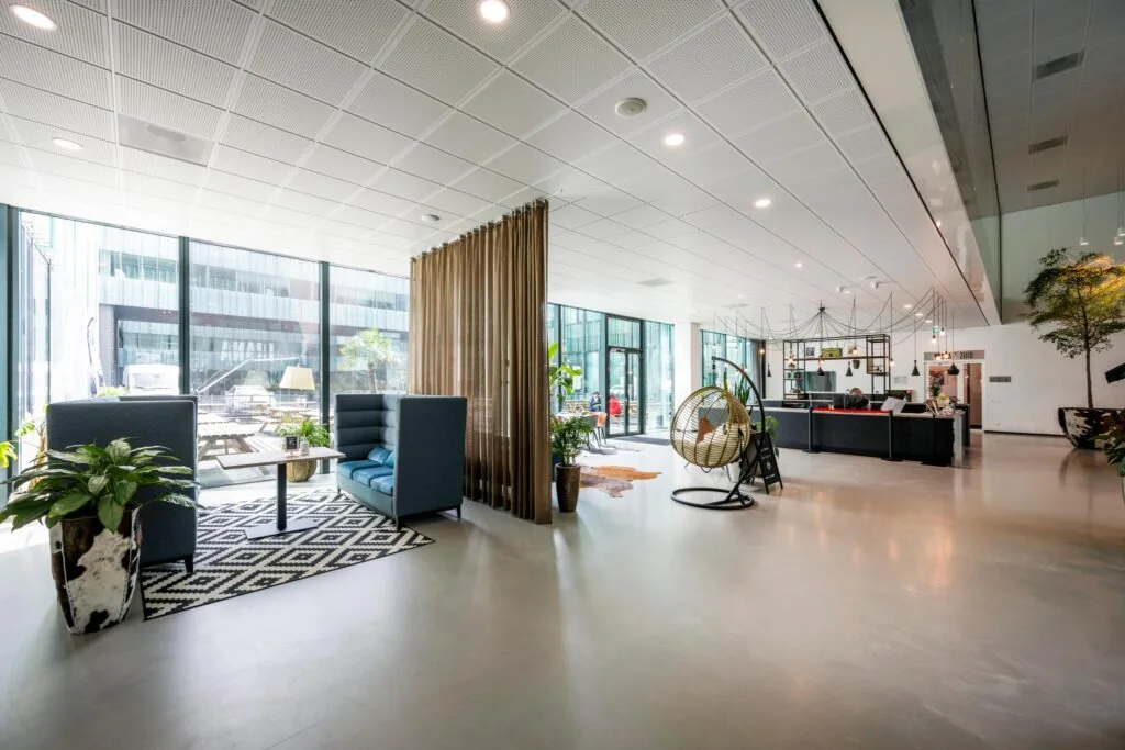 Moderne en lichte kantoorlobby aan de Herikerbergweg met zithoeken, planten en een receptiebalie.