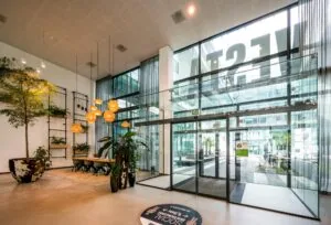 Moderne entreehal van het kantoorgebouw aan de Herikerbergweg, met glazen deuren, veel groen en hangende verlichting.