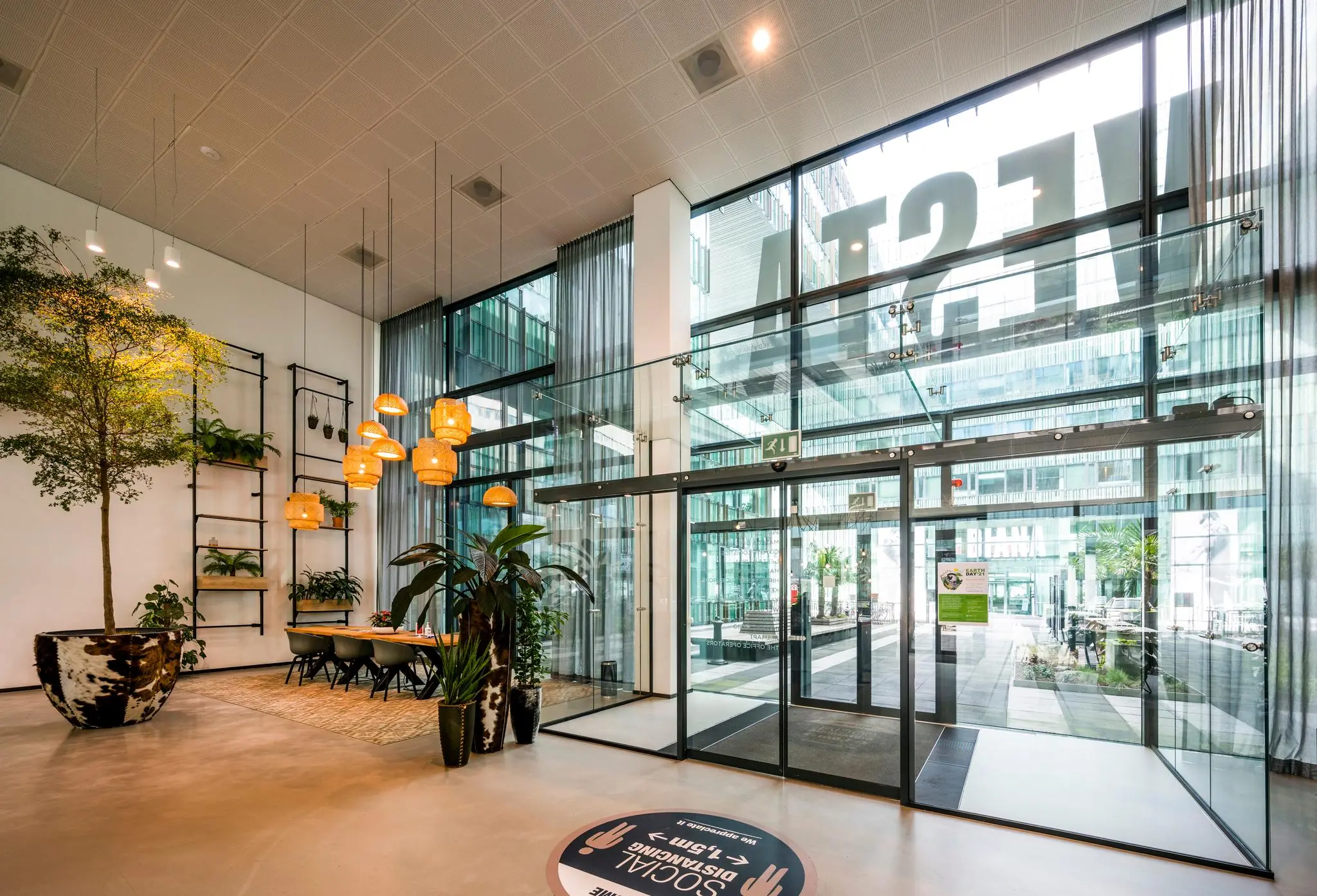 Moderne entreehal van het kantoorgebouw aan de Herikerbergweg, met glazen deuren, veel groen en hangende verlichting.