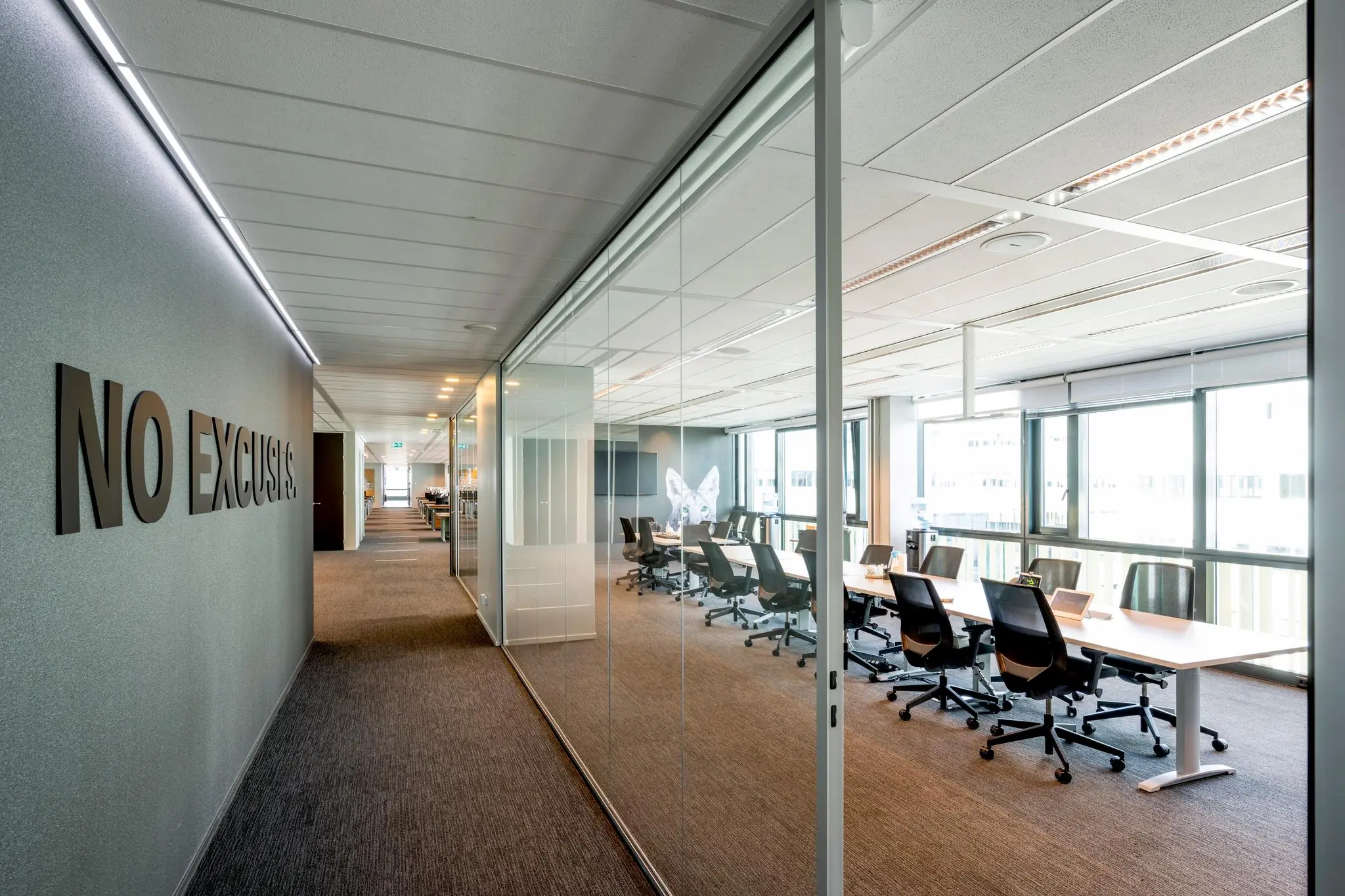 Moderne kantoorruimte aan de Herikerbergweg met glazen vergaderruimte en de tekst "NO EXCUSES" op de muur.