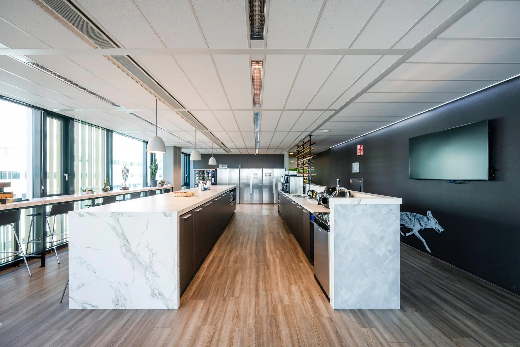 Moderne kantoorkeuken aan de Herikerbergweg met marmeren werkbladen, houten vloer en grote raampartijen.
