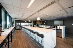 Moderne bedrijfskeuken aan de Herikerbergweg met een marmeren kookeiland, barkrukken en koffie- en snackvoorzieningen.