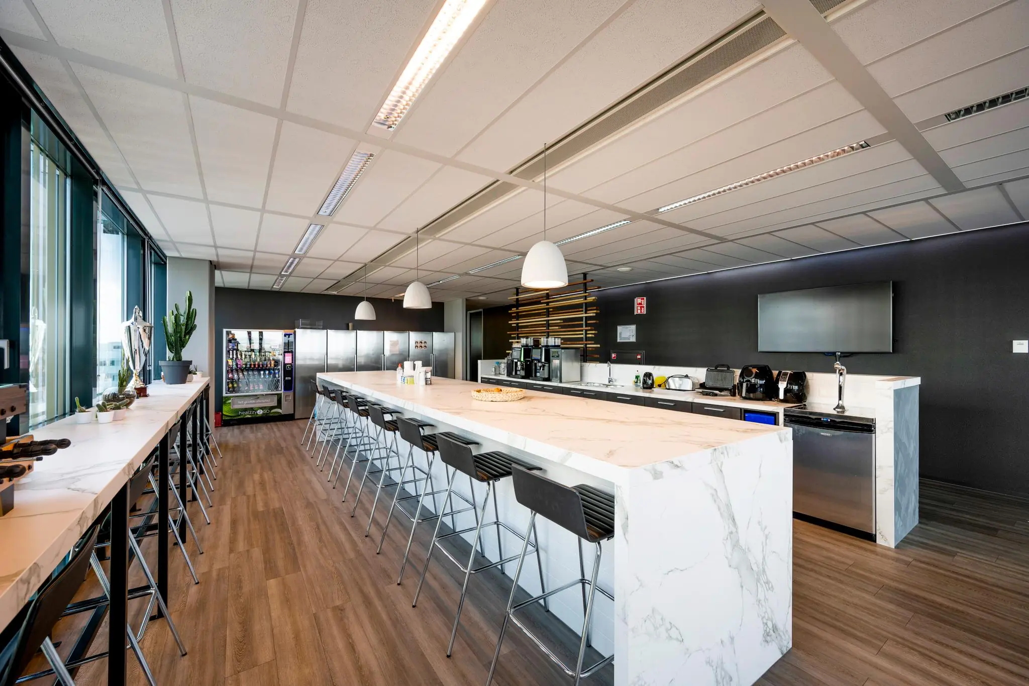 Moderne bedrijfskeuken aan de Herikerbergweg met een marmeren kookeiland, barkrukken en koffie- en snackvoorzieningen.
