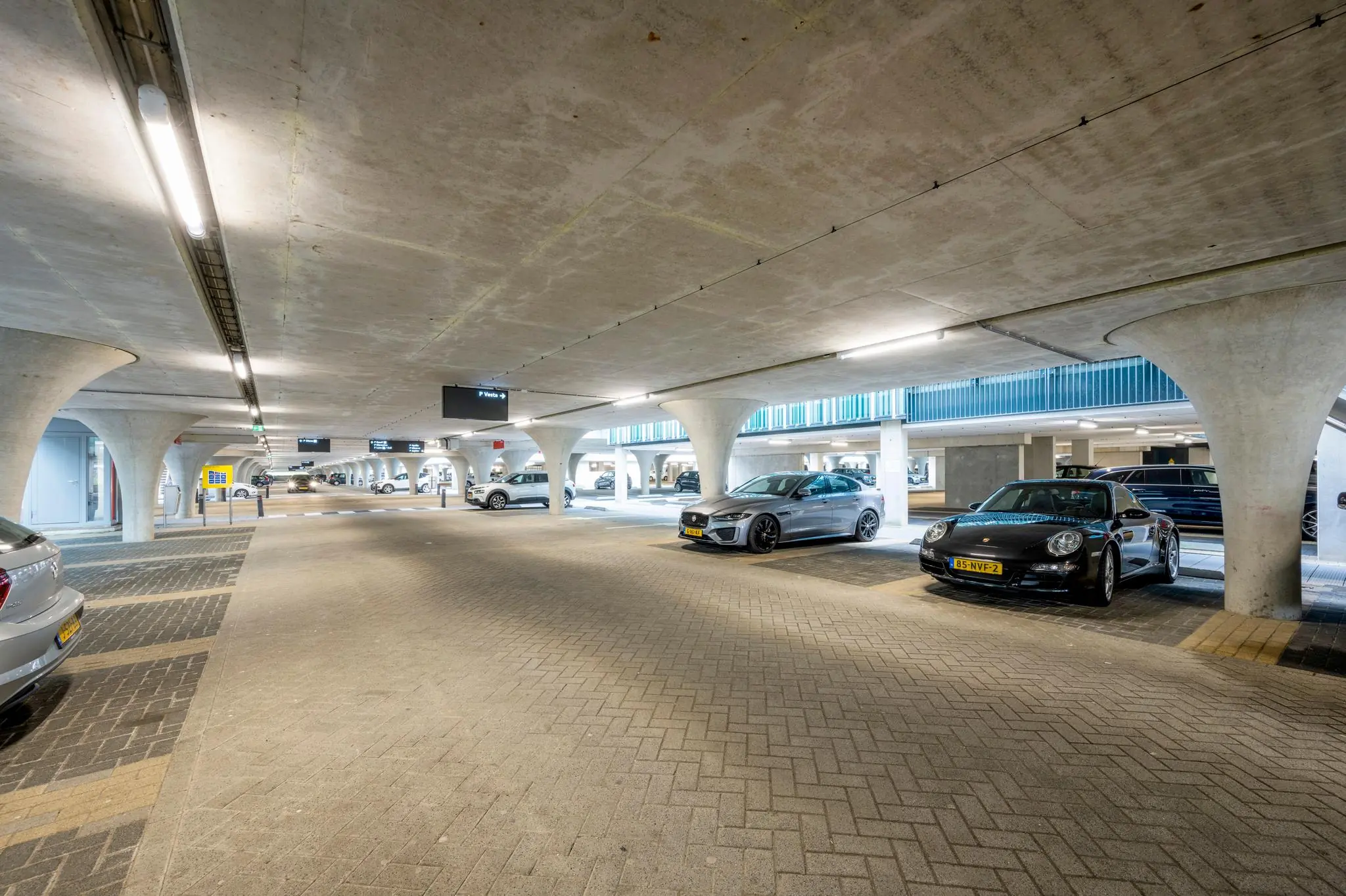 Moderne en goed verlichte parkeergarage aan de Herikerbergweg met geparkeerde auto's en betonnen zuilen.