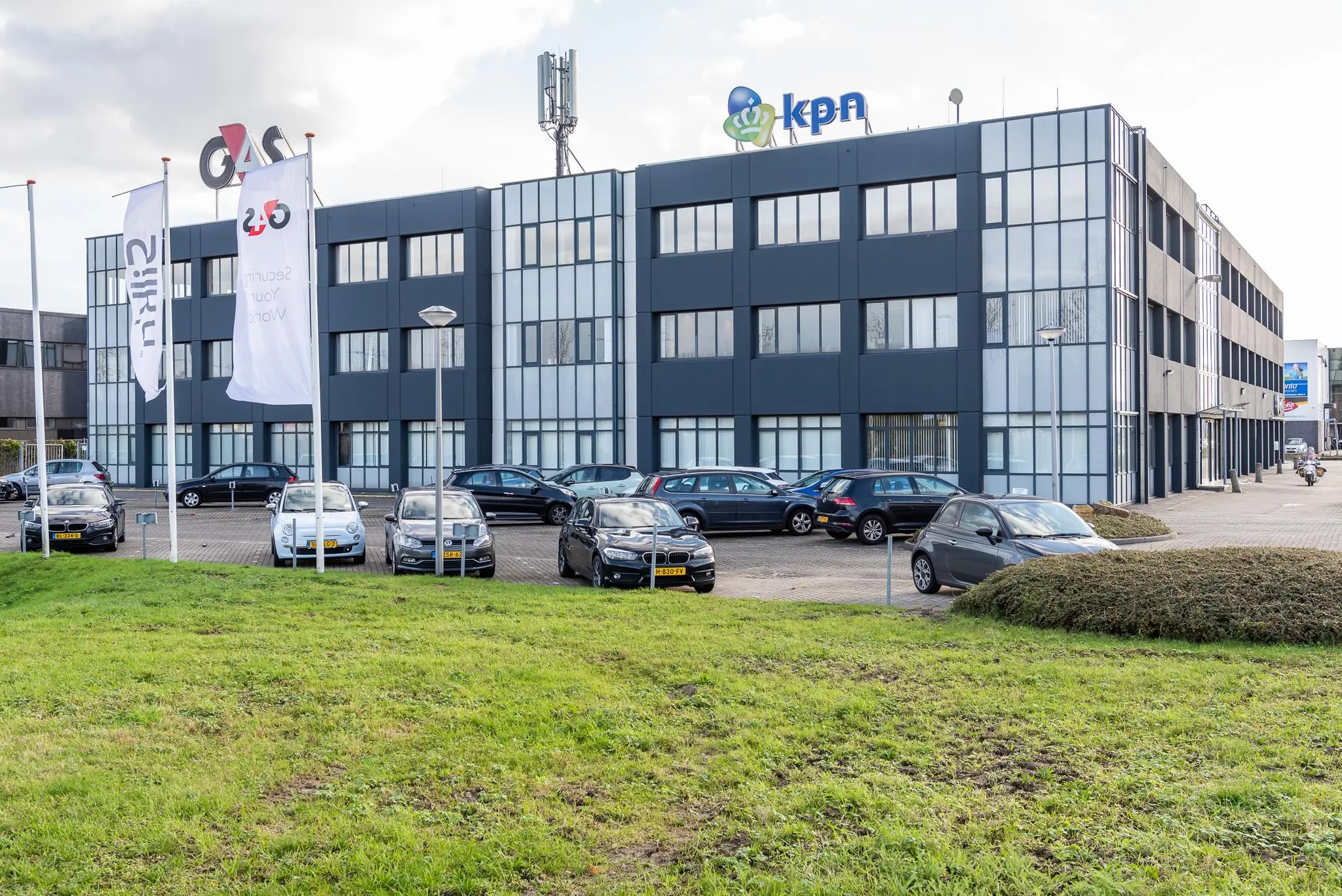 Kantoorpand met KPN- en G4S-logo's op de gevel en geparkeerde auto's op de voorgrond.