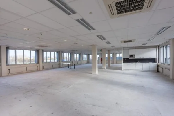 Leegstaand, ruim kantoorpand met veel ramen en een keukenblok aan de rechterzijde.