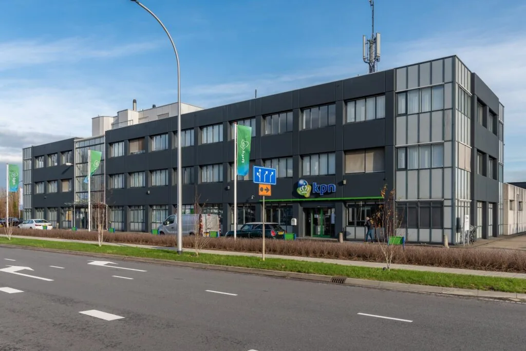 Voorgevel van een modern kantoorgebouw van KPN aan een brede weg met groenstrook en vlaggen.