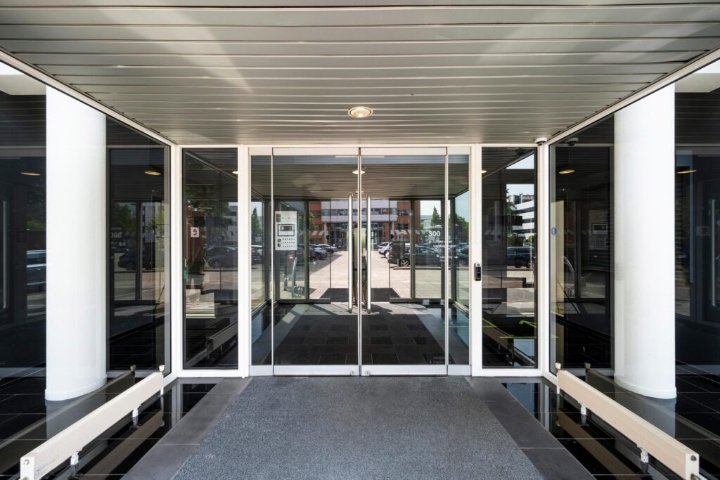 Glazen entreedeur van een modern kantoorpand met zicht op de parkeerplaats en omgeving.