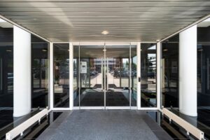 Glazen entreedeur van een modern kantoorpand met zicht op de parkeerplaats en omgeving.