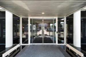 Glazen entreedeur van een modern kantoorpand met zicht op de parkeerplaats en omgeving.