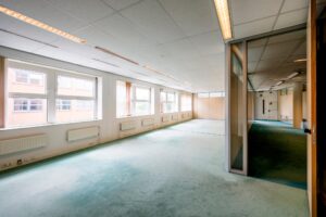 Licht en ruim kantoor met grote ramen, systeemplafond en groen tapijt.