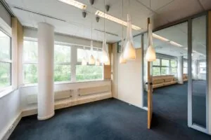 Modern kantoorinterieur met grote ramen, glazen wanden en hanglampen in een lichte vergaderruimte.