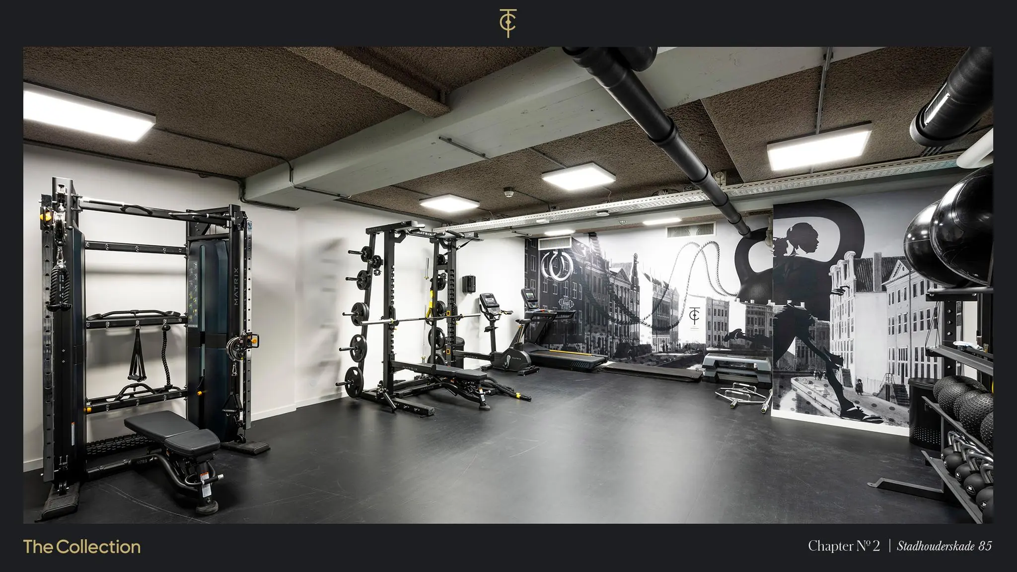 Moderne fitnessruimte aan de Stadhouderskade 85 met krachtapparatuur en een muurschildering van Amsterdamse grachtenpanden.